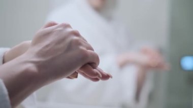 Kız ellerini krem sürmüş ve masaj yapmış, beyaz bir bornoz, banyo, el bakımı, nemlendirici cilt kremi, yakın çekim