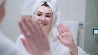 Neşeli serbest yazar eve yakın çekim için geliyor. Mutlu kız banyoda bir video görüşmesi yapıyor. Sanal sohbet sırasında bornozlu kadın el sallıyor.