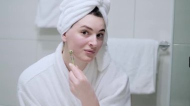 Beyaz havlulu genç bir kadın yeşim bir silindirle kendine masaj yapıyor..