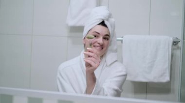 Beyaz havlulu genç bir kadın yeşim bir silindirle kendine masaj yapıyor..