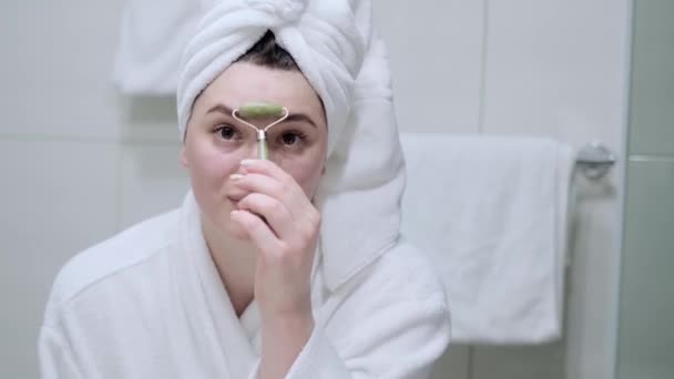 一个穿着白毛巾的年轻女子用玉筒按摩自己 — 图库视频影像