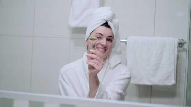 一个穿着白毛巾的年轻女子用玉筒按摩自己 — 图库视频影像