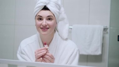 Ellerinde ruj tutan ve dudaklarını boyayan genç bir kadın sabaha hazırlanıyor. Aynada kendine bakıyor ve gülümsüyor. Makyaj yapan kadın. Randevu için hazırlan..
