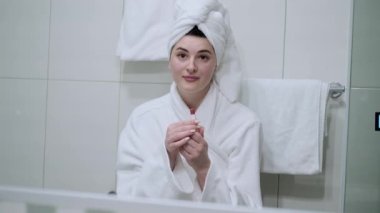 Ellerinde ruj tutan ve dudaklarını boyayan genç bir kadın sabaha hazırlanıyor. Aynada kendine bakıyor ve gülümsüyor. Makyaj yapan kadın. Randevu için hazırlan..