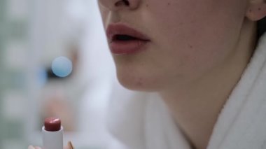 Ellerinde ruj tutan ve dudaklarını boyayan genç bir kadın sabaha hazırlanıyor. Aynada kendine bakıyor ve gülümsüyor. Makyaj yapan kadın. Randevu için hazırlan..