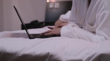 Dizüstü bilgisayarda çalışan kız. Yatak odasındaki beyaz önlüklü kadın yatakta yatıyor ve iki eli dizüstü bilgisayarın klavyesinde. kaybet-up