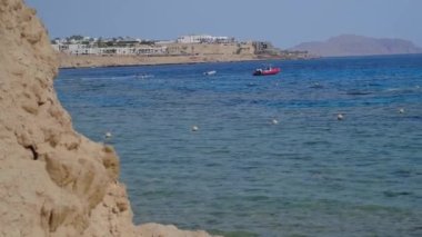 Körfezde sakin deniz suyu, yakınlarda yüzen şamandıralar, uzakta hareket eden bulanık tekne.