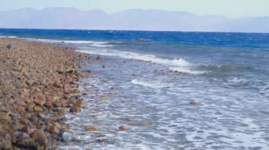 Kızıl Deniz kıyısında güçlü deniz dalgaları kopuyor. Fırtına sırasında dalgalar çakıl taşı plajına çarpar. Denizde fırtına. Kızıl Deniz 'in panoramik manzarası