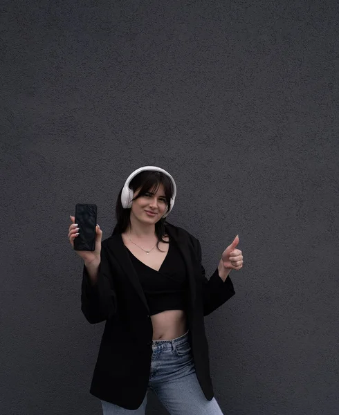 Una Adolescente Muestra Teléfono Inteligente Escucha Música Auriculares Aislados Sobre — Foto de Stock
