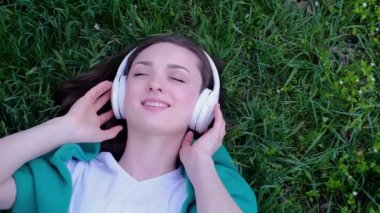 Rahatlamış bir kadın çimenlerde uzanıp parkta kulaklıkla müzik dinliyor.