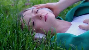 Rahatlamış bir kadın çimenlerde uzanıp parkta kulaklıkla müzik dinliyor.