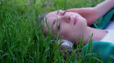 Rahatlamış bir kadın çimenlerde uzanıp parkta kulaklıkla müzik dinliyor.
