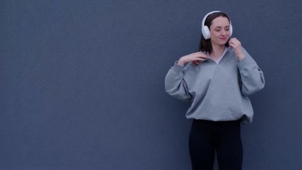 全身上下的白人女孩穿着耳机听音乐 在灰色背景下跳舞 — 图库视频影像