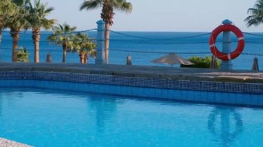 Havuzda can simidi var. Önünde bir havuz var, arkasında da deniz ve hurma ağaçları. Lüks bir otelde güvenli bir tatil.