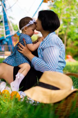 Güzel anne ve tatlı kızı parkta çilek ve mandalina yiyorlar ve piknik günlerinin, aile hafta sonlarının, park tatillerinin tadını çıkarıyorlar.