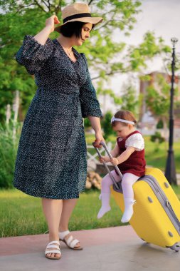 Seyahat konsepti: bavullu anne ve kız bir yolculuğa hazırlanıyor, bir çocuk bavula biniyor, bir anne bir çocuğu bavula sarıyor, denizde tatil yapıyor, ailesiyle seyahat ediyor.