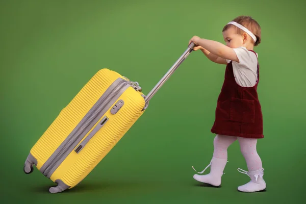 stock image A little joyful cute girl in a blue summer dress and a straw hat holds a yellow suitcase. Vacation, holidays, trip to the sea, space for text, go on vacation