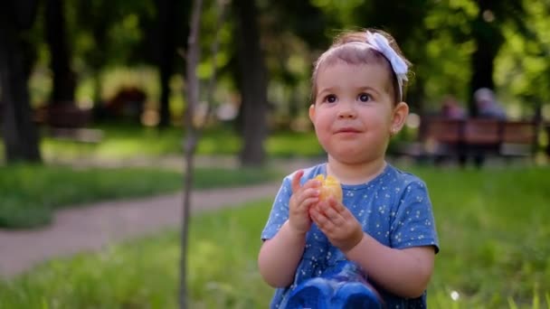 一个小孩坐在操场上荡秋千 吃着橙子 给孩子们使用维生素 孩子们的多种维生素 橙汁顺着胳膊流下来 像一条蓝鱼一样摆动着 — 图库视频影像