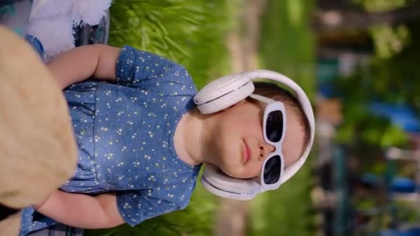 一个咀嚼着耳机听音乐 在公园里跳舞的小孩 坐在草地上打开的行李箱里 准备度假旅行 — 图库视频影像