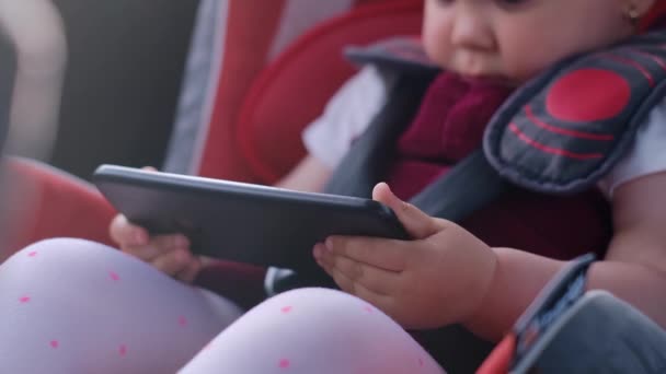 小さな子供がデジタルタブレットを使って車の座席に座って車で移動しながら画面上の漫画を見ています 子供の車の中での子供の気晴らしの概念 安全な輸送 — ストック動画