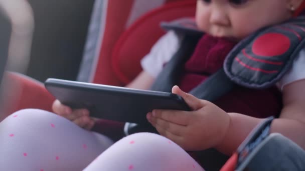 一个小孩坐在车座上使用数字平板电脑 一边开车一边在屏幕上看卡通片 儿童在汽车分心中的概念 安全的交通工具 — 图库视频影像
