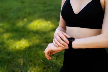 Akıllı saat, kulaklıklar ve parkta koşan sonuçları, antrenman ilerleyişini ve hedefleri olan fitness kadını. Açık hava eğitimi için akıllı saati ve müzik ekipmanı olan genç koşucu ya da sporcu kız