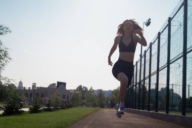 Spor giyimli bir kadın spor stadyumunda çalışıyor. Açık havada koşan zinde bir kadın. Sabahleyin ısınma turu. Sağlıklı ve aktif yaşam tarzı konsepti, fitness silueti, gün doğumu, koşma sağlık egzersizi