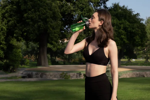 公園でジョギングしながら若い女の子は水を飲む 健康的な週末 ヒップスターフィットネスティーンエイジャーは屋外でジョギングした後きれいな新鮮な水を飲む 健康的なライフスタイル — ストック写真