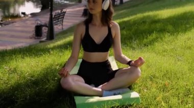 Genç bir kadın bahçede yoga yapıyor. Sağlıklı yaşam tarzı ve rahatlama konsepti. Genç bir kız parkta yoga yapıyor. Meditasyon, doğanın keyfi.