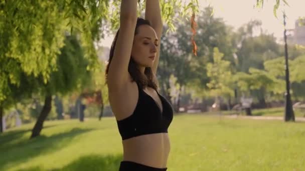 在一个被大自然环绕的公园里 一个女孩在绿草上摆出一个荷花的姿势 享受瑜伽和健康生活方式的锻炼 小女孩在公园的绿草上做瑜伽 享受大自然 — 图库视频影像