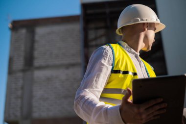 İnşaat mühendisi tablet kullanıyor, bir proje planlıyor, modern bir yapı inşa ediyor, bir plan okuyor. İnşaat alanında çalışan mimar veya mühendis.