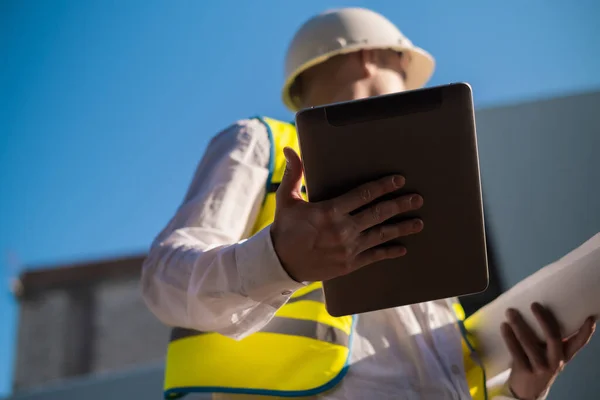 Civil engineer using a tablet, planning a project, builds a modern structure, reading a plan. Architect or engineer working on a construction site.
