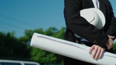 İnşaat alanının arka planına miğfer tutan bir mühendisin yakın çekimi. İnşaatçı ya da müteahhit inşaatın gidişatını kontrol eder. Koruyucu kask