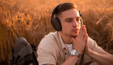 Rahat adam temiz hava soluyor ve kulaklıkla müzik dinlerken meditasyon yapıyor, yakışıklı genç adam kulaklıkla müzik dinliyor, çimenlerde dinleniyor.