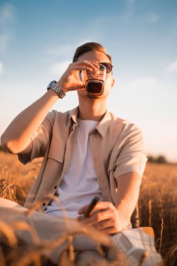 Bir adamın elinde nefis bir alkollü içecek. Çiftçi bira üreticisi taze birayı olgun bir tarlada taşır.