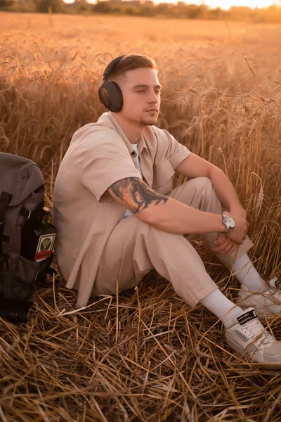 Relaxed man breathes fresh air and meditates while listening to audio guide on headphones in nature, Handsome young man listens to music on headphones, relaxes on the grass