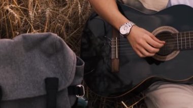 Erkek hipster buğday tarlasında elektro gitarla oynuyor. Uzun saçlı hippi adam arpa otlağında müzik aleti çalıyor. Genç adam doğada dinleniyor. Arka planda güzel bir gün batımı. Yavaş çekim