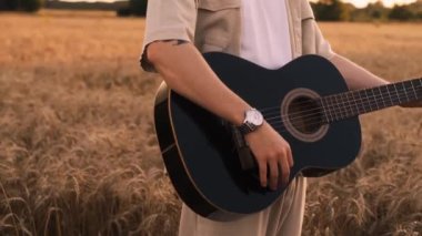 Erkek hipster buğday tarlasında elektro gitarla oynuyor. Uzun saçlı hippi adam arpa otlağında müzik aleti çalıyor. Genç adam doğada dinleniyor. Arka planda güzel bir gün batımı. Yavaş çekim
