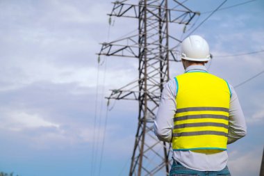 Erkek mühendis, miğferdeki güç mühendisi online tablet kullanarak güç hattını kontrol ediyor. Dışarıdaki elektrikçi. Gün batımında yüksek voltajlı elektrik hatları. Elektrik dağıtımı ve arzı