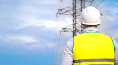 Erkek mühendis, miğferdeki güç mühendisi online tablet kullanarak güç hattını kontrol ediyor. Dışarıdaki elektrikçi. Gün batımında yüksek voltajlı elektrik hatları. Elektrik dağıtımı ve arzı
