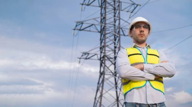 Kasklı ve güvenlik gözlüklü beyaz erkek mühendis, cep telefonu tesislerini kontrol eden telekomünikasyon kulesinin yanında saha çalışması için akıllı telefon kullanıyor..