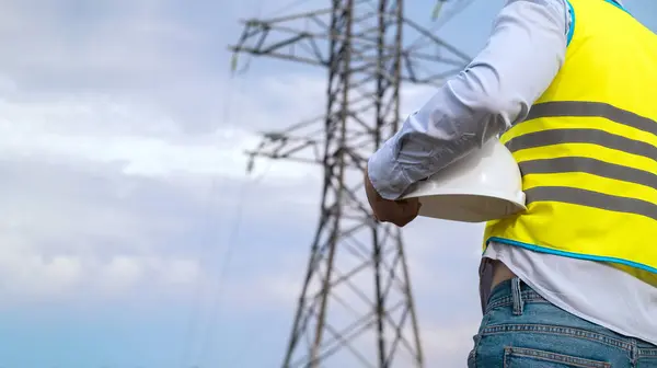 A male power engineer in a white helmet checks a power line using data from electrical sensors on a tablet. High voltage electrical lines at sunset. Distribution and supply of electricity. clean energy