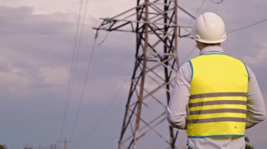 Tablet bilgisayar, elektrik hatları ve direklere sahip kontrol mühendisi, köy ve kasabalar için genişleme planı ve enerji naklini tartışıyor.