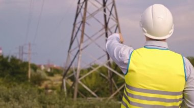 Tablet bilgisayar, elektrik hatları ve direklere sahip kontrol mühendisi, köy ve kasabalar için genişleme planı ve enerji naklini tartışıyor.