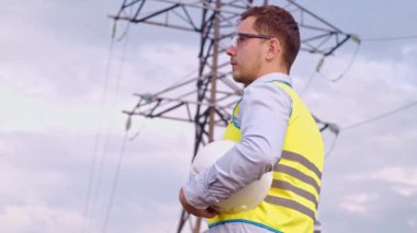 Bir tasarımcı yüksek voltaj kulesini kontrol eder. Bir güç iletim pilonuna hizmet eden kasklı bir mühendis. Güç hattında kask takan bir elektrik mühendisi. Bir tasarımcı yüksek voltaj sensörünü kontrol eder