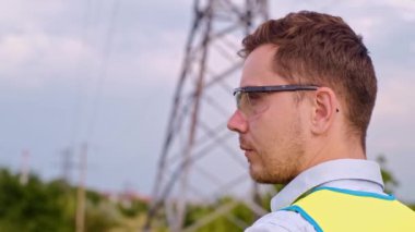 Bir tasarımcı yüksek voltaj kulesini kontrol eder. Bir güç iletim pilonuna hizmet eden kasklı bir mühendis. Güç hattında kask takan bir elektrik mühendisi. Bir tasarımcı yüksek voltaj sensörünü kontrol eder