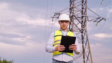 Bir tasarımcı yüksek voltaj kulesini kontrol eder. Bir güç iletim pilonuna hizmet eden kasklı bir mühendis. Güç hattında kask takan bir elektrik mühendisi. Bir tasarımcı yüksek voltaj sensörünü kontrol eder