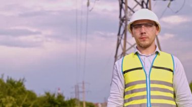 Bir tasarımcı yüksek voltaj kulesini kontrol eder. Bir güç iletim pilonuna hizmet eden kasklı bir mühendis. Güç hattında kask takan bir elektrik mühendisi. Bir tasarımcı yüksek voltaj sensörünü kontrol eder