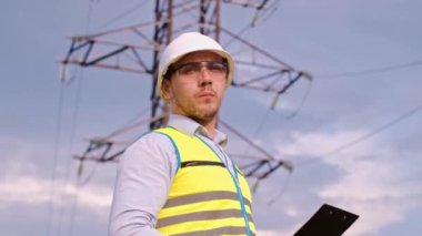 Bir tasarımcı yüksek voltaj kulesini kontrol eder. Bir güç iletim pilonuna hizmet eden kasklı bir mühendis. Güç hattında kask takan bir elektrik mühendisi. Bir tasarımcı yüksek voltaj sensörünü kontrol eder