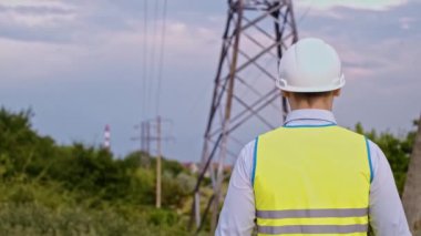 Bir tasarımcı yüksek voltaj kulesini kontrol eder. Bir güç iletim pilonuna hizmet eden kasklı bir mühendis. Güç hattında kask takan bir elektrik mühendisi. Bir tasarımcı yüksek voltaj sensörünü kontrol eder